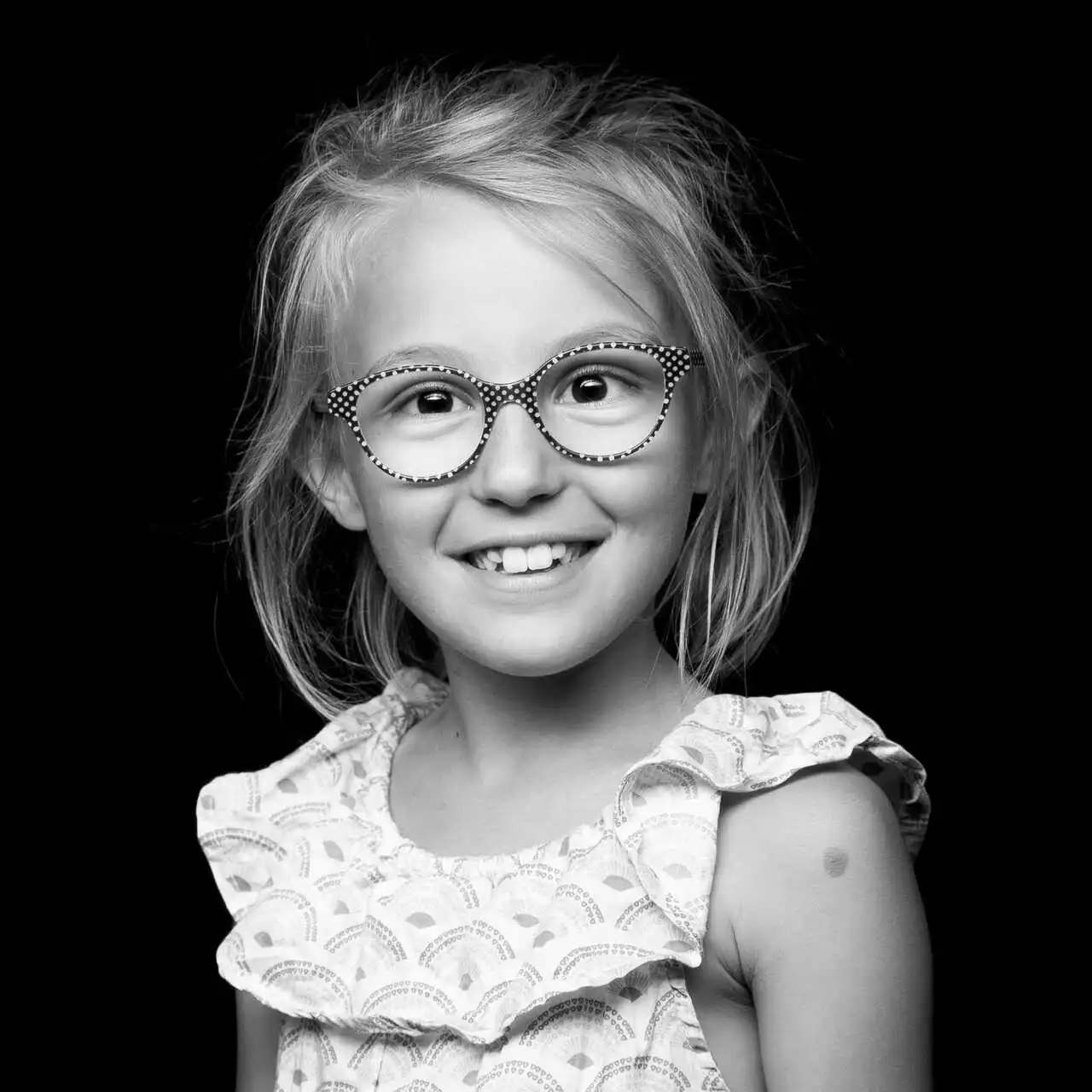 Portrait en noir et blanc d'une jeune fille souriante portant des lunettes, illustrant la joie et la positivité des témoignages recueillis par BigBizYou pour le livre d'ASRL.