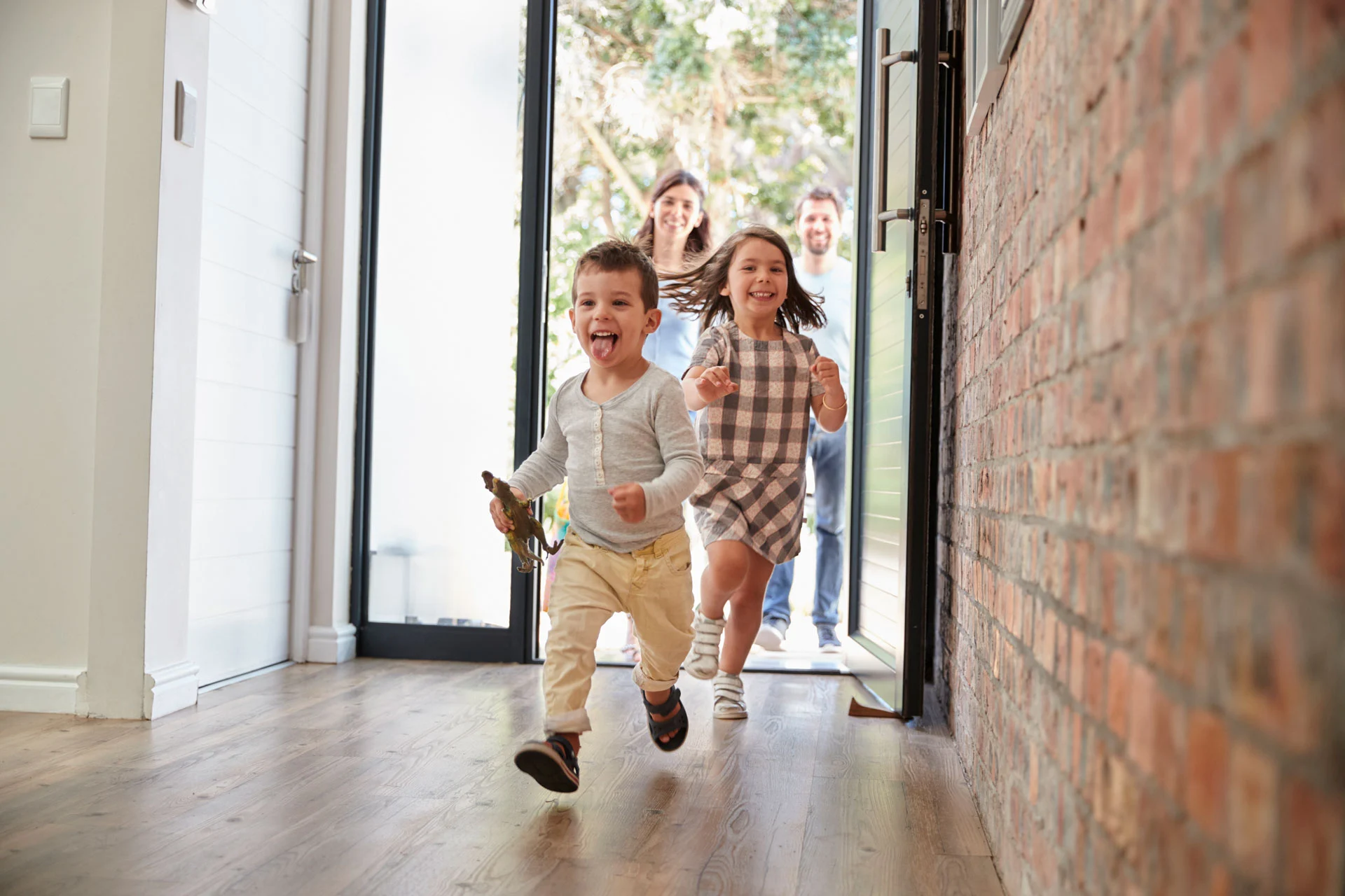 Une famille joyeuse franchissant le seuil de sa maison, symbole du bien-être apporté par la rénovation de menuiseries réalisée par Extembel, dont le site web a été créé par BigBizYou.